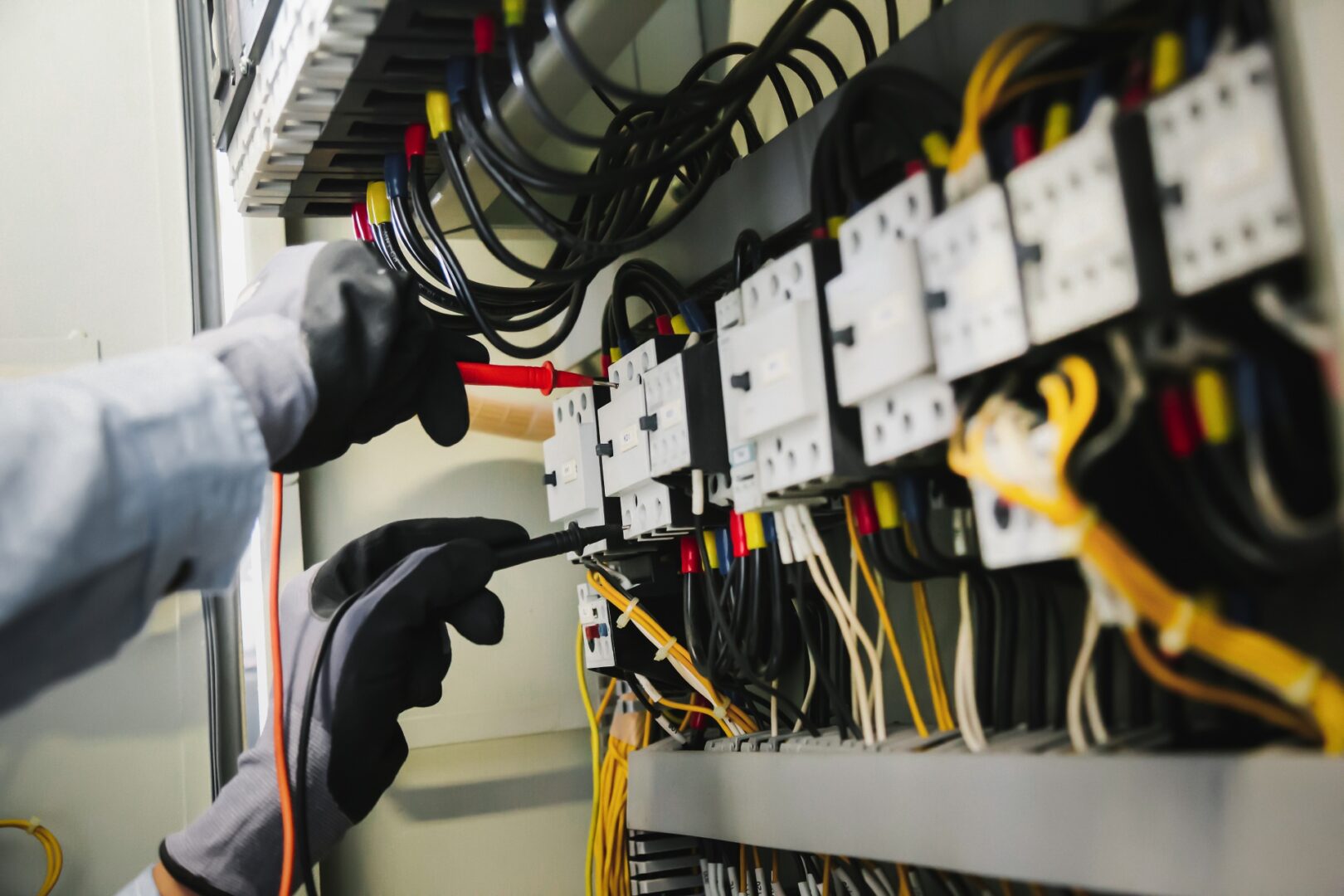 Electrician working on a circuit breaker panel with tools and gloves.